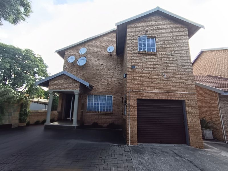 Front elevation of a double-storey face brick townhouse featuring a single garage, covered entrance porch, and paved driveway.