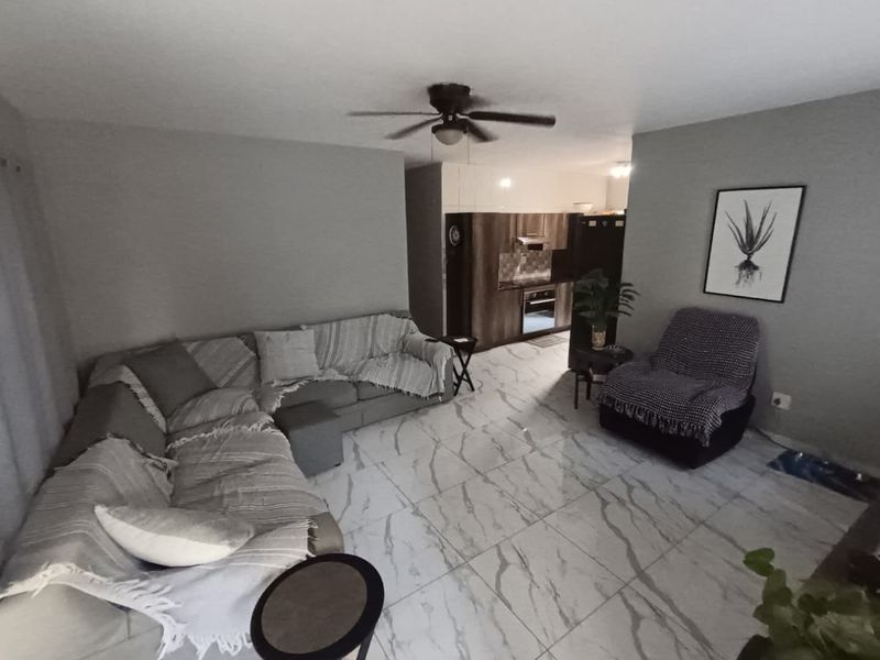Open-plan living area featuring modern marble-look floor tiles, a ceiling fan, and a compact kitchen with built-in cabinetry and appliances.