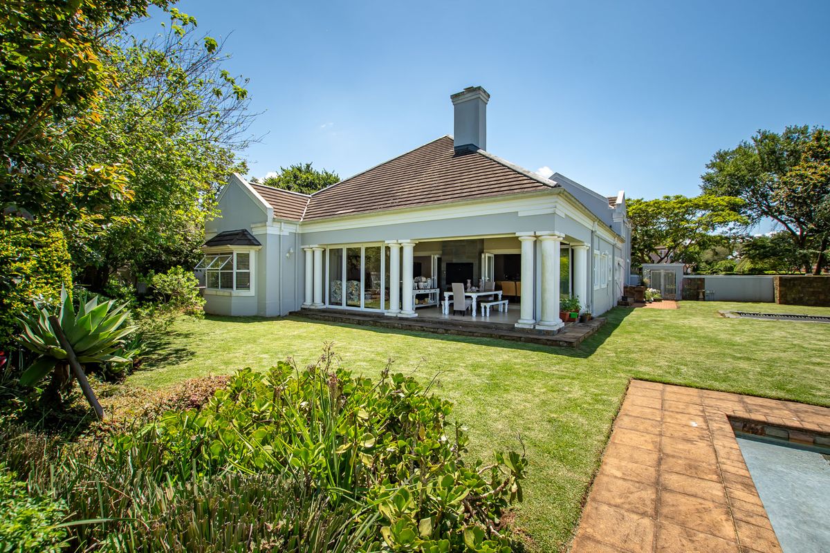 Rear view of the house featuring a spacious covered patio with classical columns, overlooking a well-maintained garden and a swimming pool.