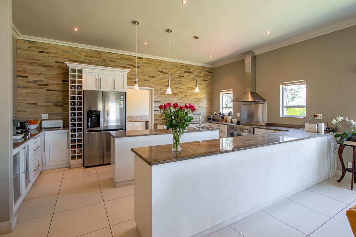 Modern kitchen featuring a stone veneer accent wall, granite countertops, a central island, and integrated stainless steel appliances with ample cabinetry.
