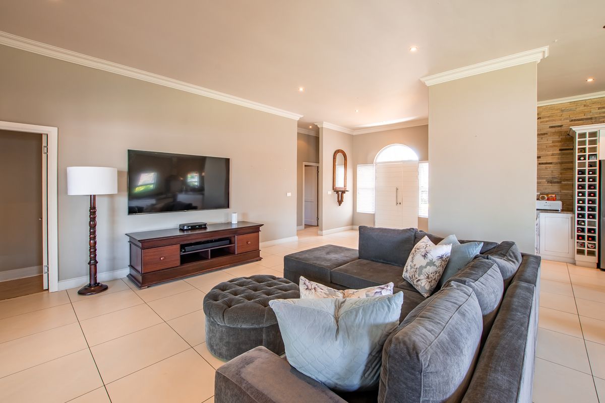 Spacious living room featuring neutral tiled flooring, recessed downlighting, crown molding, and a decorative stone feature wall in the adjacent area.