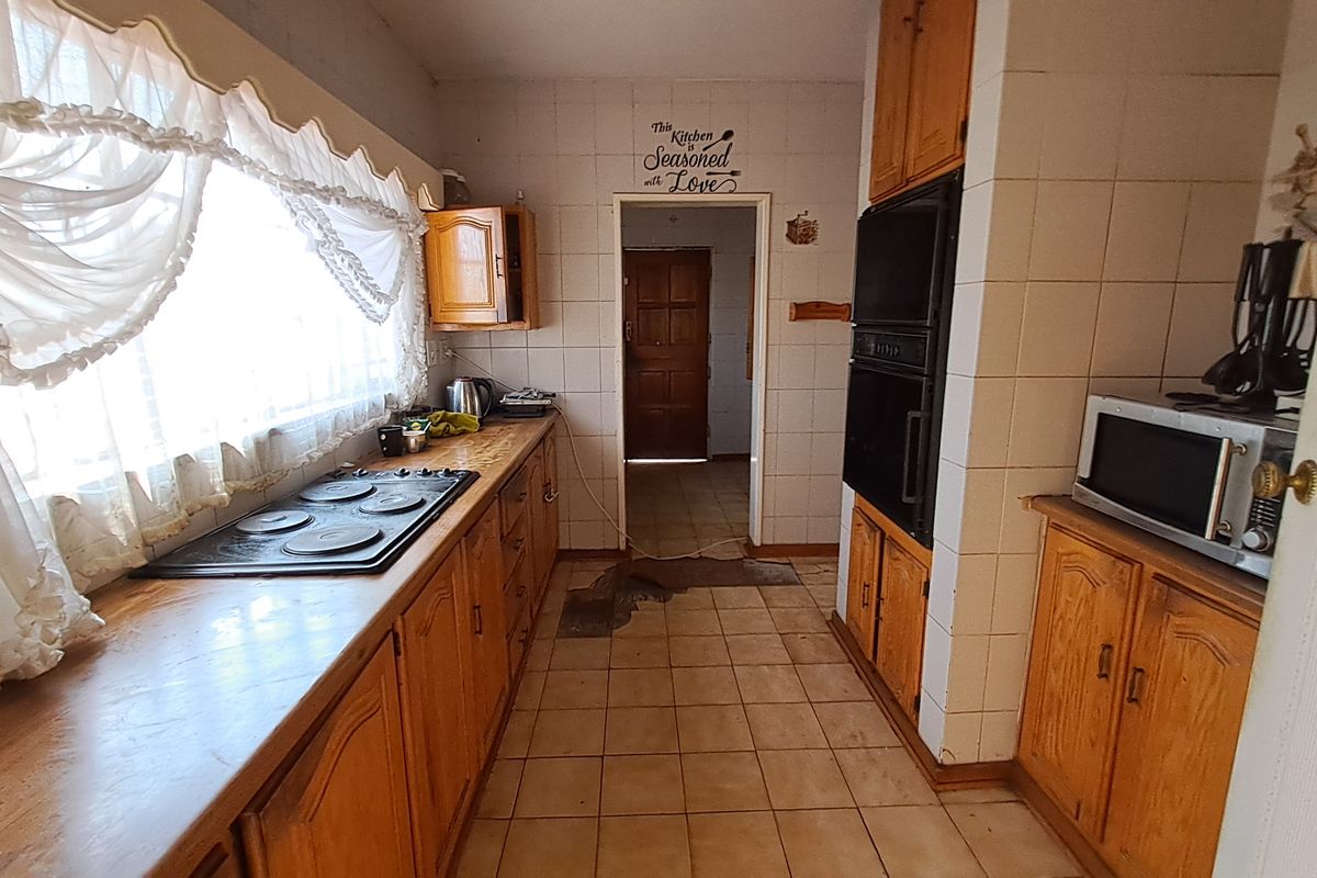 A dated kitchen featuring wooden cabinetry, built-in oven, electric hob, and tiled surfaces, offering potential for a modern renovation.