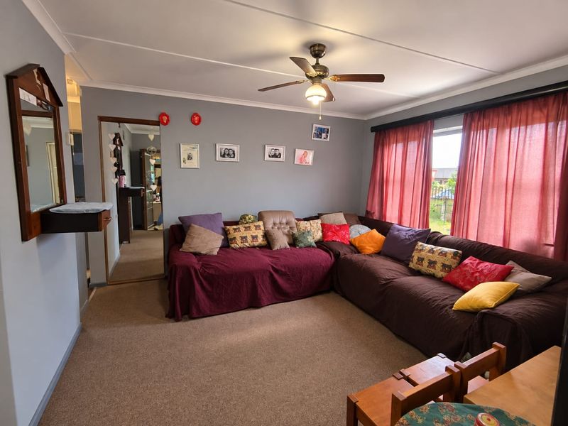 A comfortable living room featuring carpeted flooring, a ceiling fan, and coved ceilings, providing a functional and lived-in space.