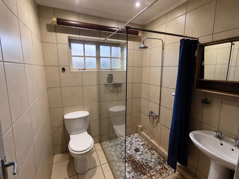 A functional bathroom featuring a pedestal basin, toilet, and a walk-in shower with a glass screen and tiled finishes.