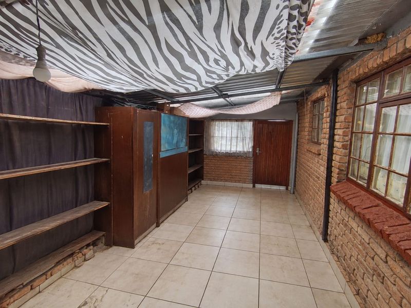 A covered outdoor patio area featuring exposed brick walls, tiled flooring, and a corrugated metal roof structure.