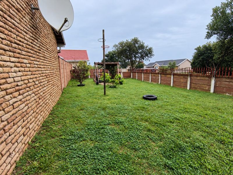 A spacious rear garden featuring a lawn, enclosed by a combination of brick and precast concrete boundary walls.