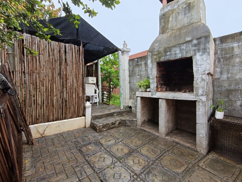 Outdoor patio area featuring a built-in masonry braai, paved flooring, and a shaded structure, offering potential for an upgraded entertainment space.
