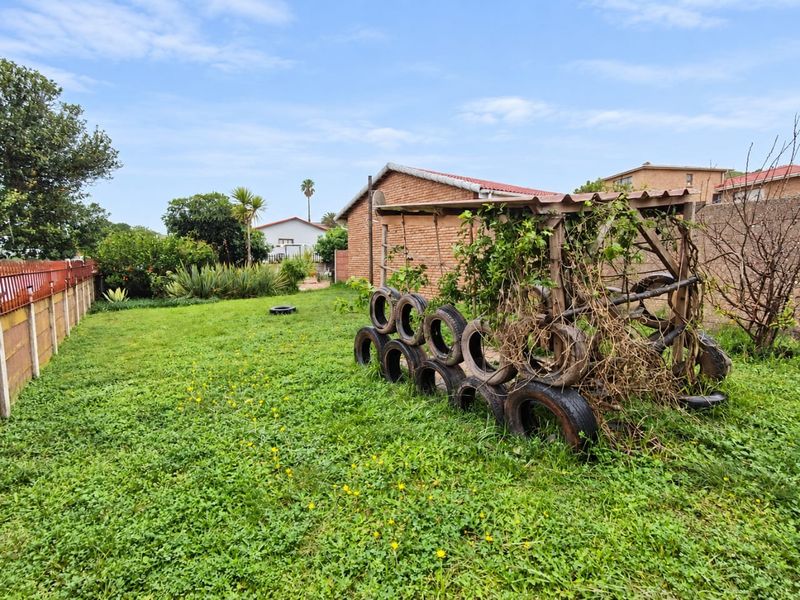 A spacious backyard garden featuring a lawn, brick boundary walls, and a neglected wooden structure with climbing plants.