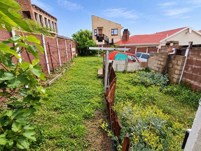A rear garden area featuring a precast concrete boundary wall, metal washing line, and established vegetation, requiring landscaping and maintenance.