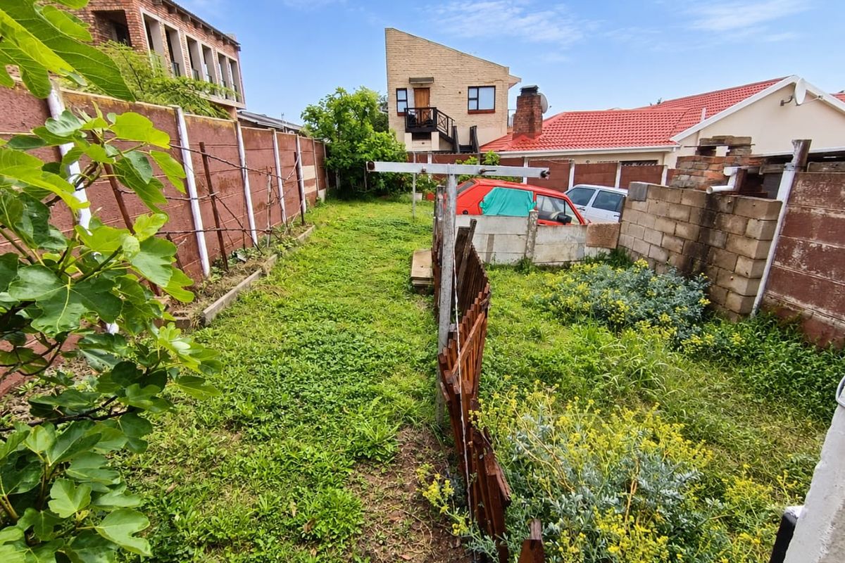 A rear garden area featuring a precast concrete boundary wall, metal washing line, and established vegetation, requiring landscaping and maintenance.