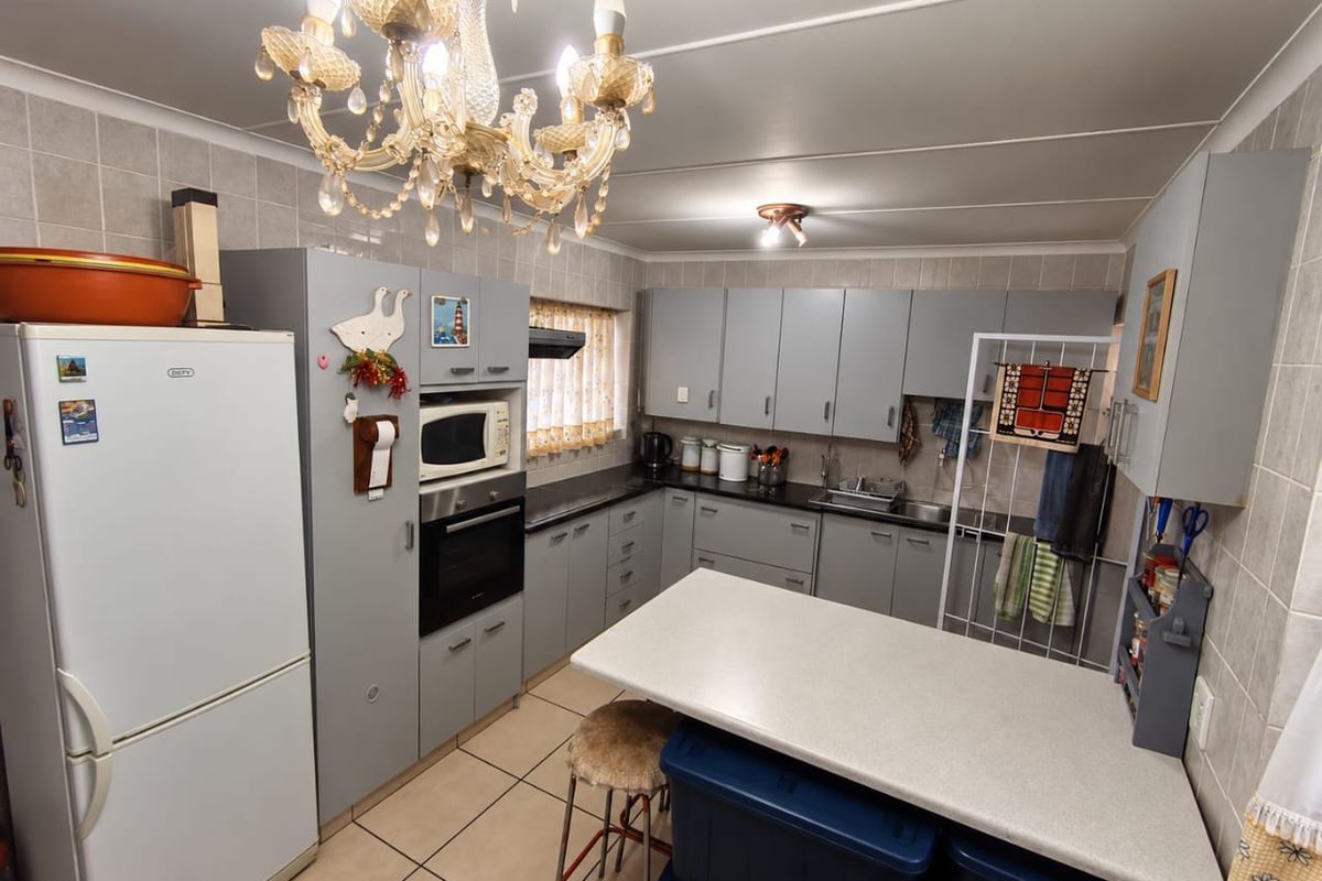 A functional kitchen featuring grey cabinetry, laminate countertops, built-in oven, extractor fan, and tiled finishes throughout.