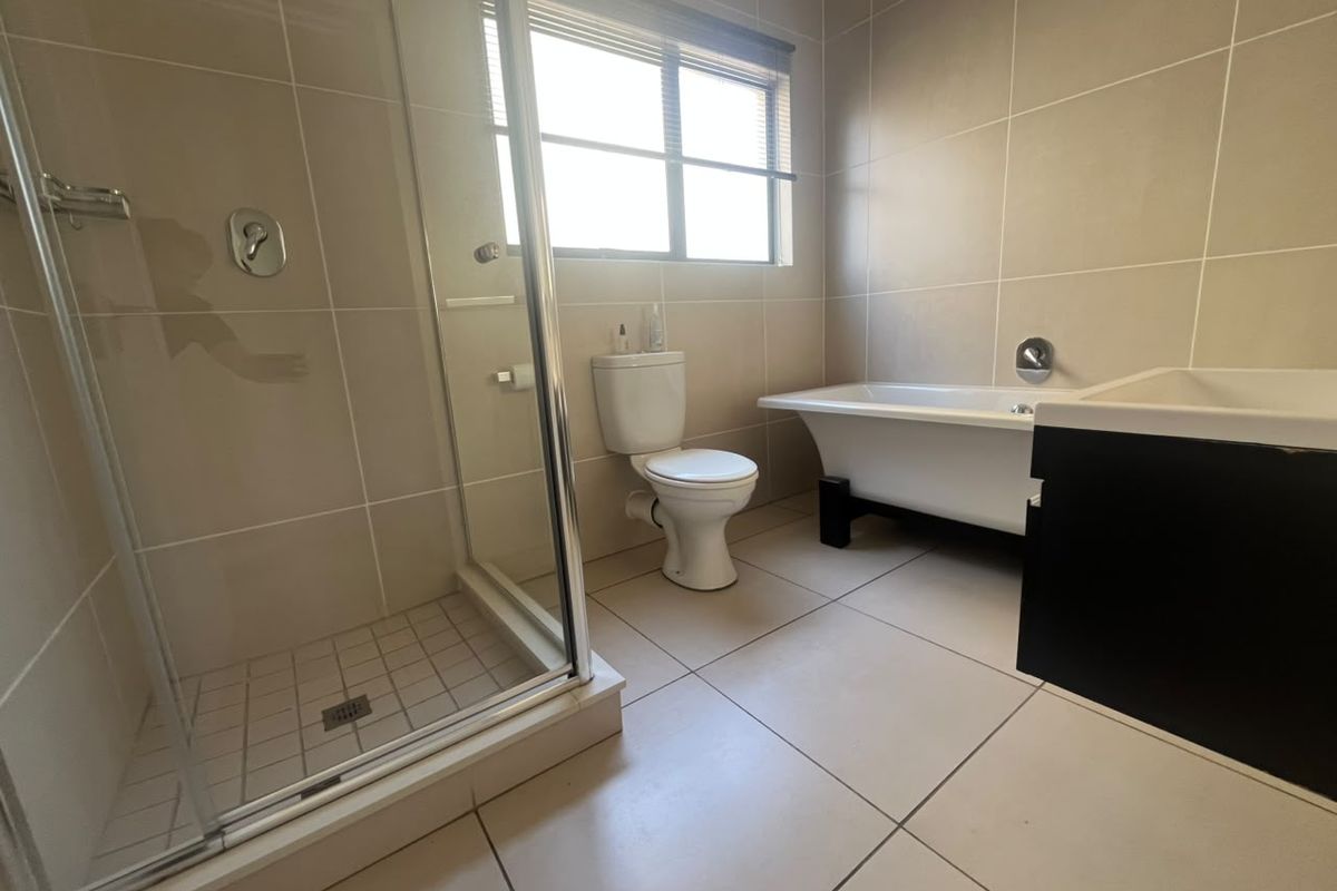 A clean, modern bathroom featuring a glass shower enclosure, a freestanding bathtub, a toilet, and a wall-mounted vanity with neutral floor and wall tiling.
