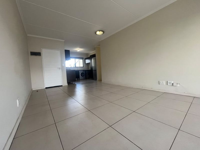 An open-plan living and kitchen area featuring neutral tiled flooring, built-in cabinetry, and a clean, minimalist layout ready for personalization.