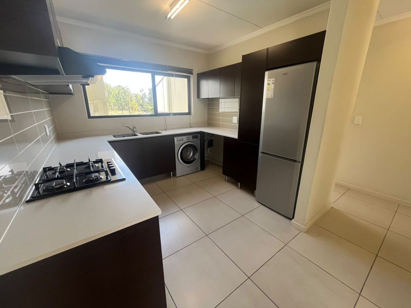 Modern kitchen featuring dark wood cabinetry, white countertops, a gas hob with extractor, and integrated space for laundry appliances.