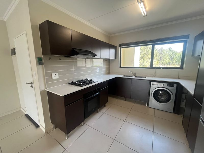 Modern kitchen featuring dark wood cabinetry, stone countertops, gas hob, built-in oven, and integrated laundry plumbing in a clean, tiled space.
