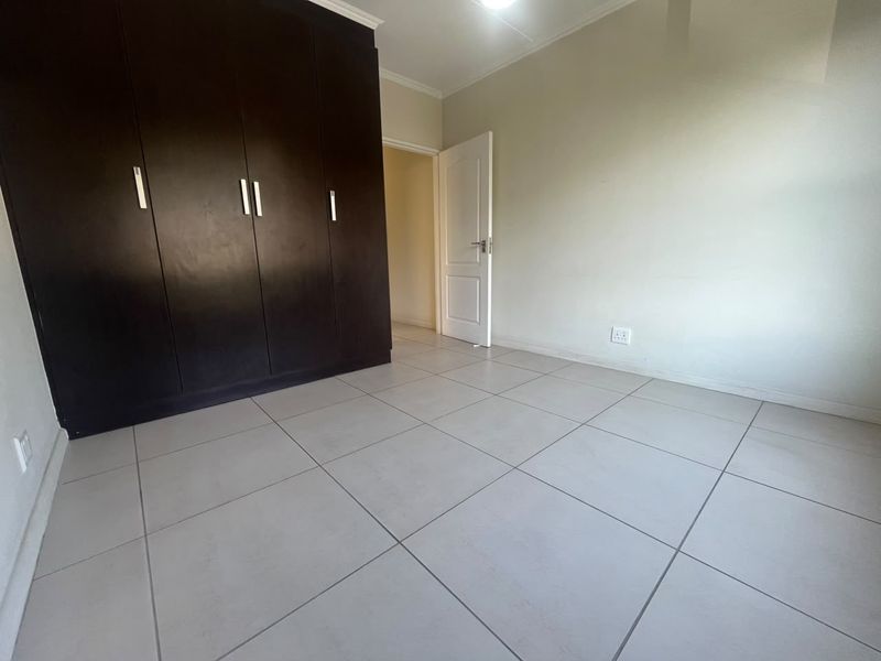 A clean, empty bedroom featuring neutral tiled flooring and dark built-in cupboards, offering a blank canvas for personalization.