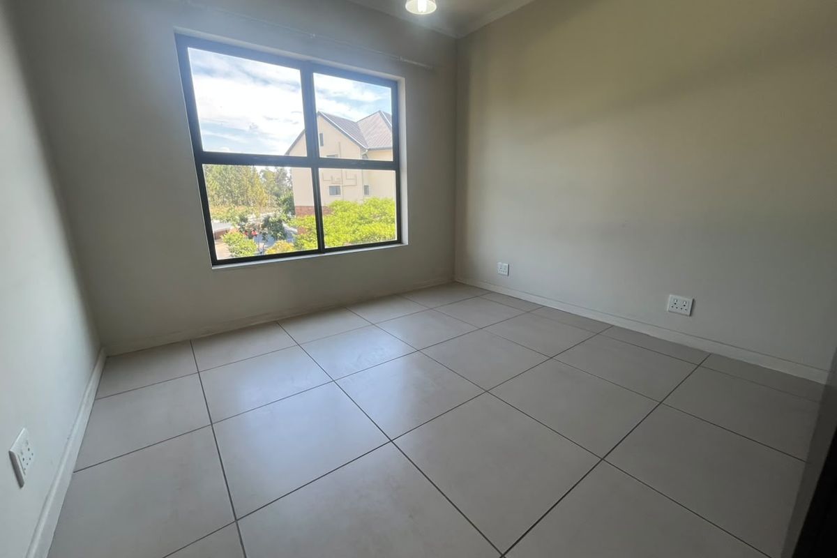 A bright, empty bedroom featuring neutral tiled flooring, a large window providing natural light, and clean wall finishes.