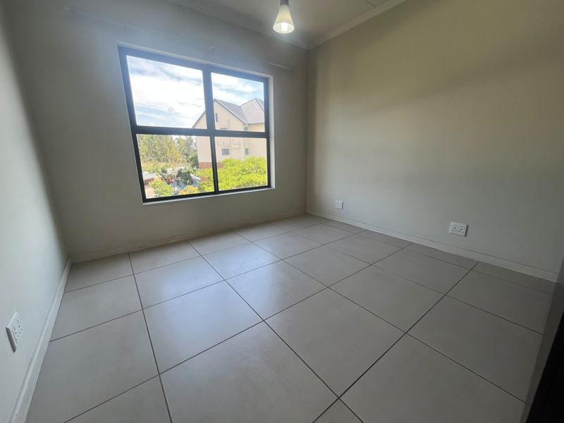 A bright, empty bedroom featuring neutral tiled flooring, a large window providing natural light, and clean wall finishes.