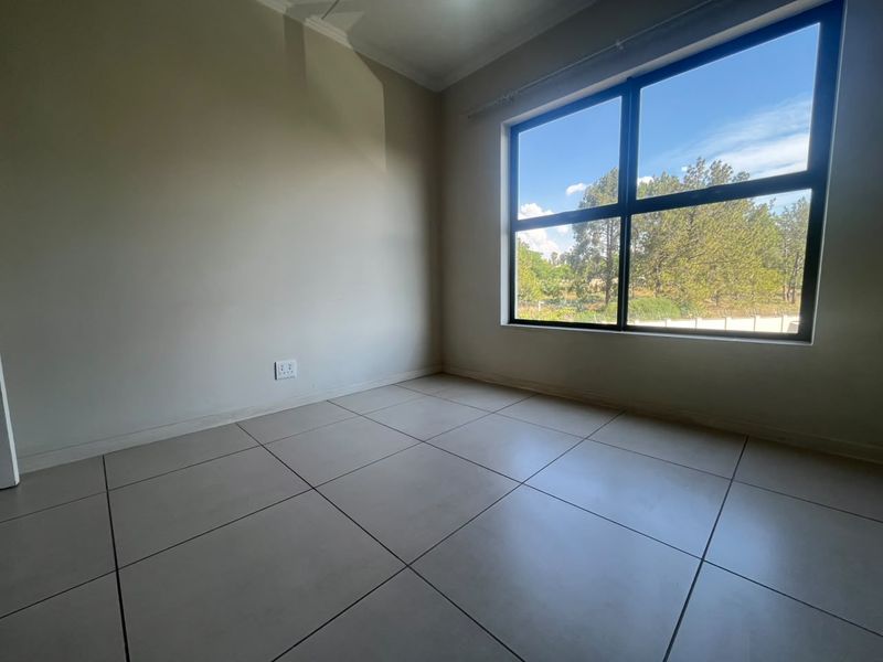 A bright, empty bedroom featuring large aluminium-framed windows, neutral tiled flooring, and clean wall finishes, offering a blank canvas for personalization.