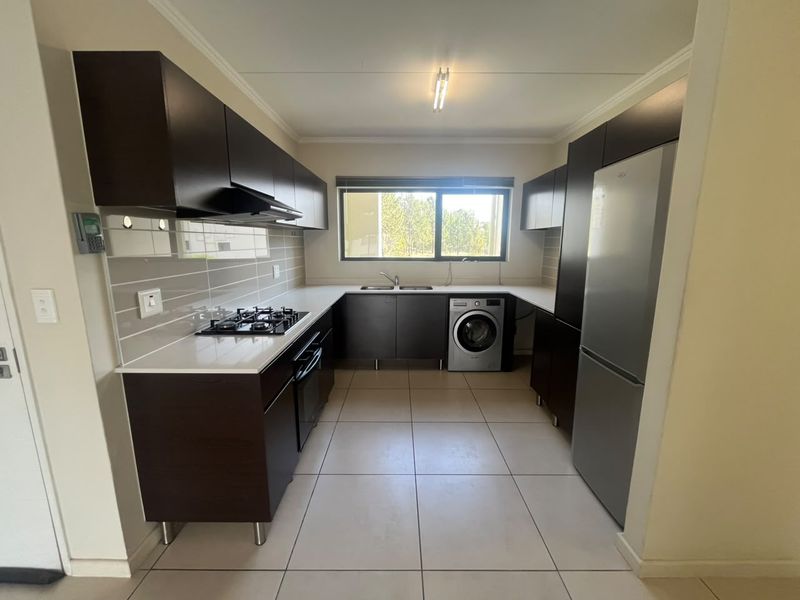 Modern kitchen featuring dark wood cabinetry, stone countertops, gas hob, extractor fan, and integrated space for a washing machine and fridge.