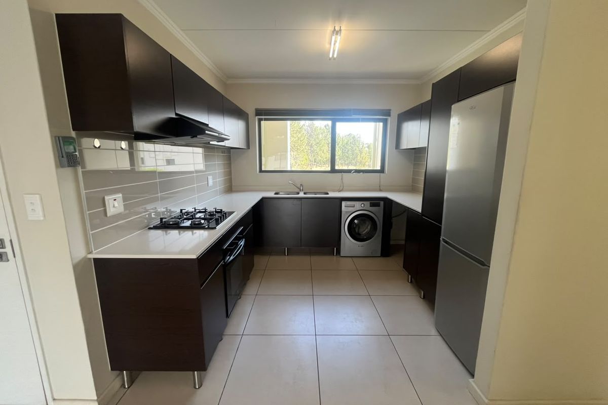 Modern kitchen featuring dark wood cabinetry, stone countertops, gas hob, extractor fan, and integrated space for a washing machine and fridge.
