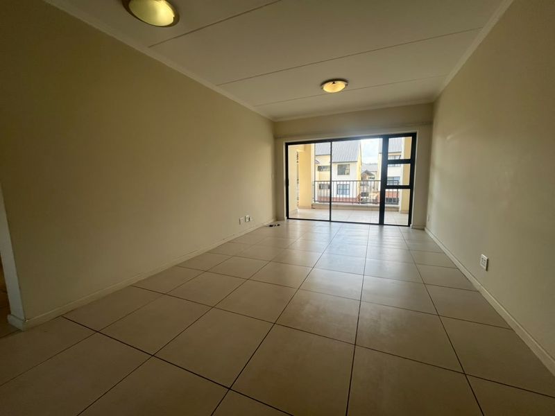 A spacious, empty living area featuring neutral tiled flooring and large sliding glass doors that provide natural light and access to a private balcony.