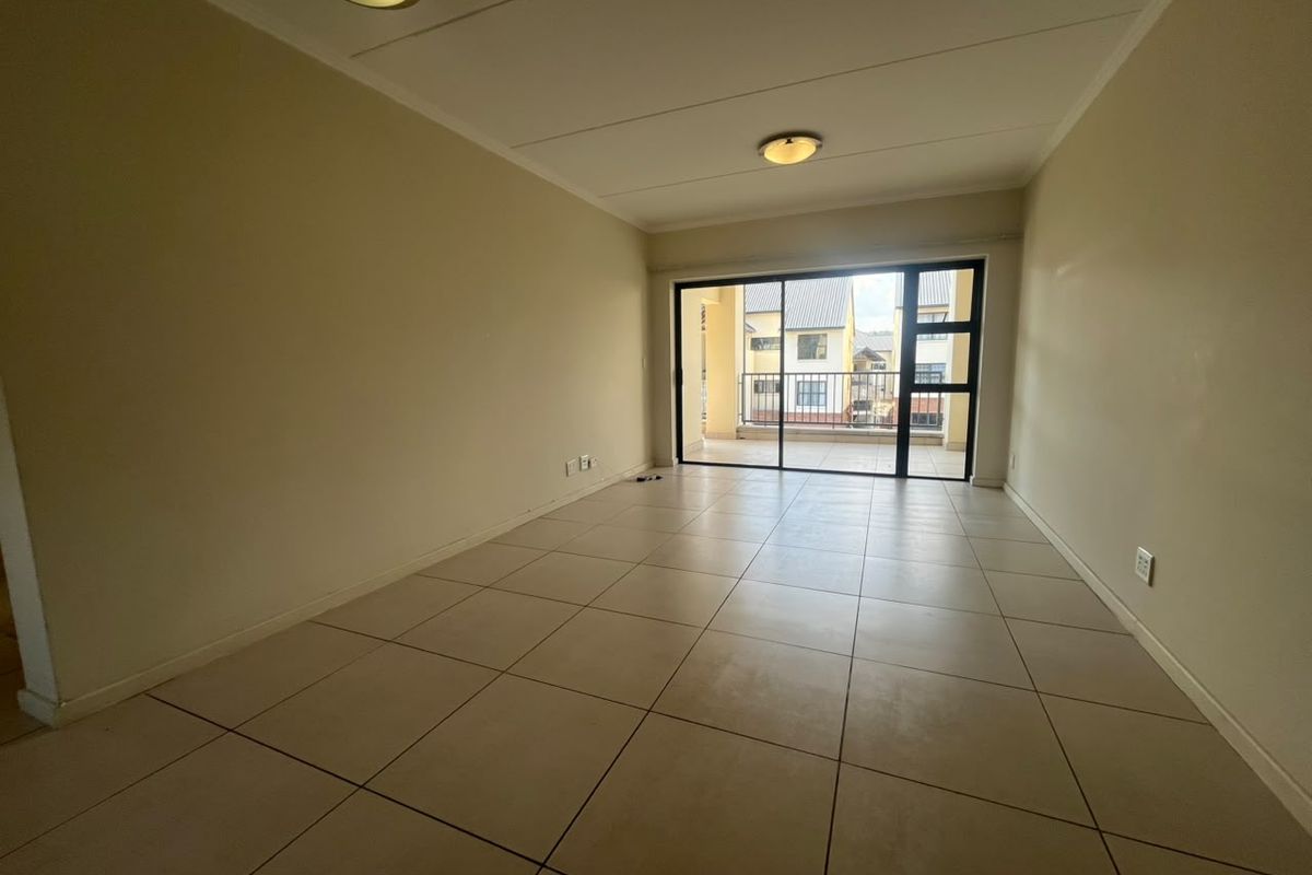 A spacious, empty living area featuring neutral tiled flooring and large sliding glass doors that provide natural light and access to a private balcony.