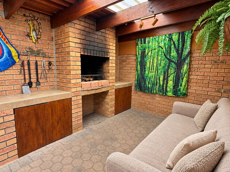 Covered outdoor patio featuring a built-in brick braai, tiled prep area with wooden cabinetry, and exposed timber beam ceiling.