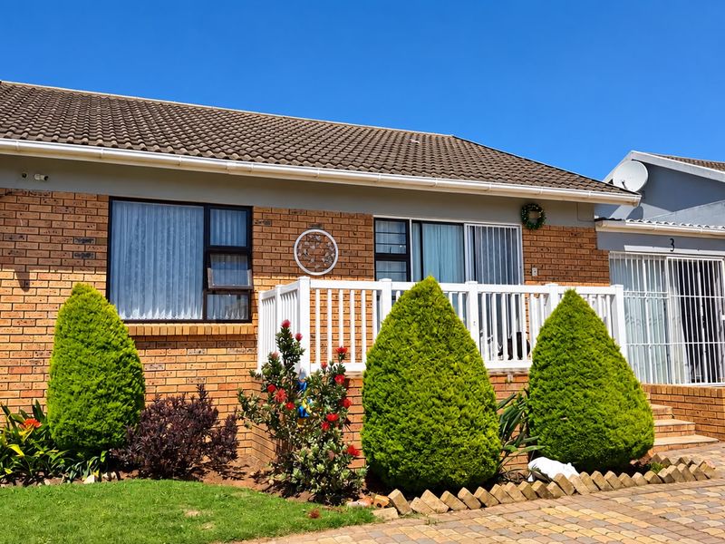 Front elevation of a brick townhouse featuring a tiled roof, white balustrade, and a paved driveway with established garden landscaping.