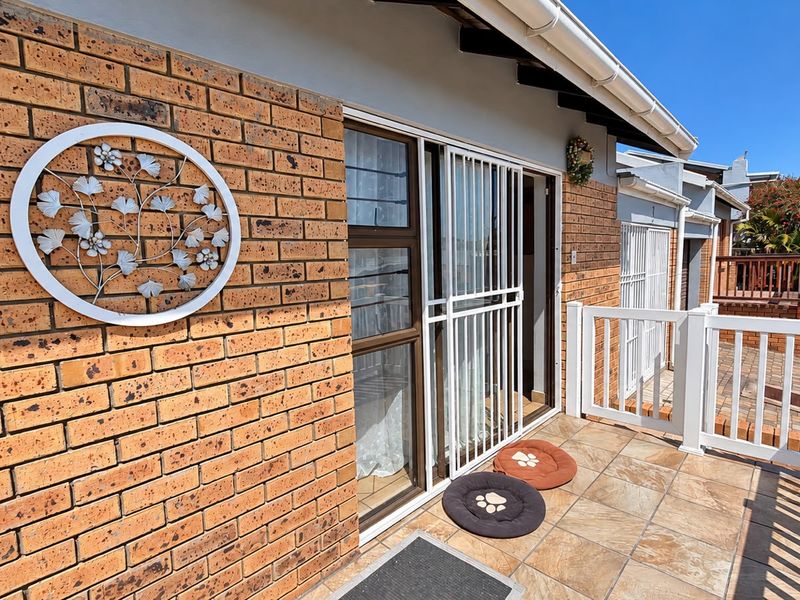 A well-maintained tiled patio area featuring face brick walls, a white metal security gate, and a protective balustrade overlooking the exterior grounds.