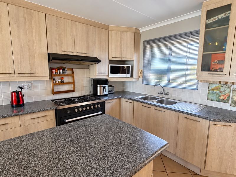 A functional kitchen featuring light wood-look cabinetry, granite countertops, a gas stove with extractor fan, and a double basin sink with tiled backsplash.