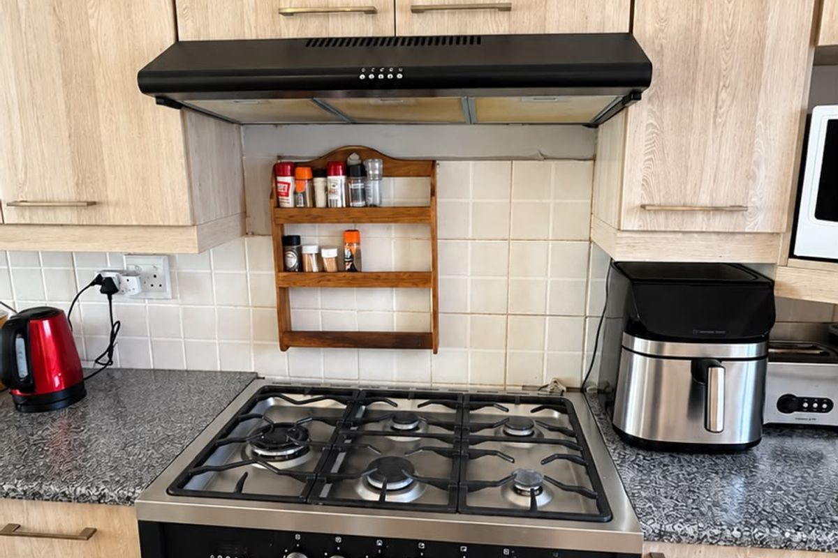 A functional kitchen area featuring light wood-finish cabinetry, granite countertops, a tiled backsplash, and a modern black gas stove with an integrated extractor fan.