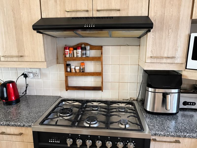 A functional kitchen area featuring light wood-finish cabinetry, granite countertops, a tiled backsplash, and a modern black gas stove with an integrated extractor fan.