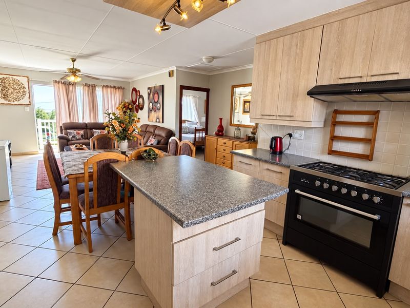 Open-plan living and kitchen area featuring light wood cabinetry, a central kitchen island, gas stove, and tiled flooring throughout the combined space.