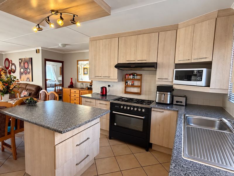 Open-plan kitchen and dining area featuring light wood cabinetry, a central island, gas stove, and tiled flooring, creating a functional and connected living space.