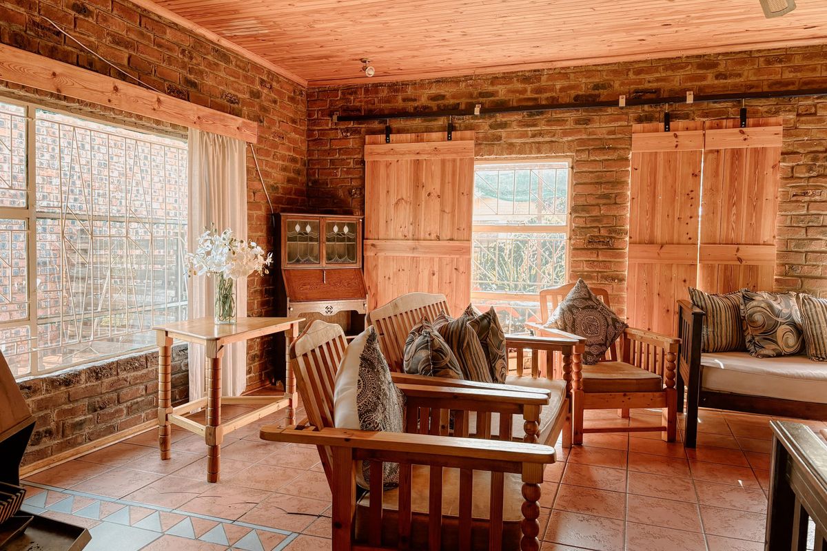 Rustic living room featuring exposed brick walls, timber-clad ceiling, tiled flooring, and sliding wooden barn-style shutters over the windows.