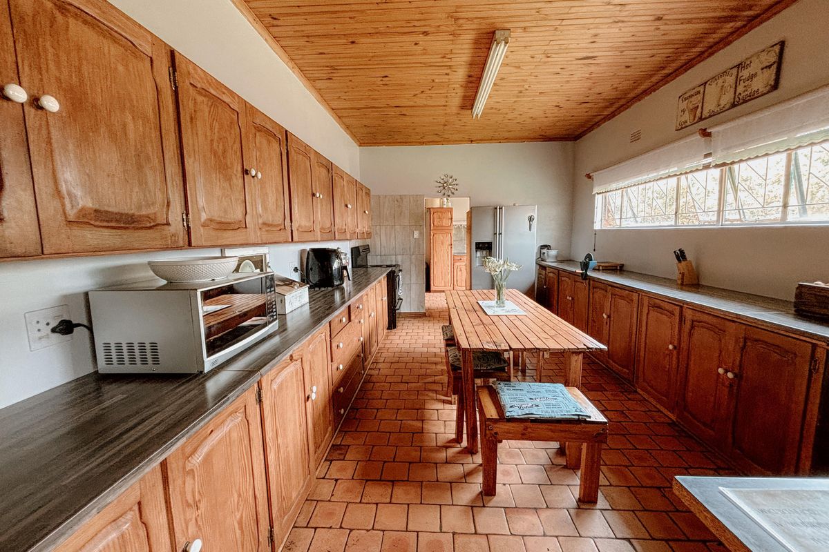 Spacious kitchen featuring extensive wooden cabinetry, terracotta tiled flooring, and a timber-clad ceiling, offering a traditional aesthetic with ample storage and workspace.