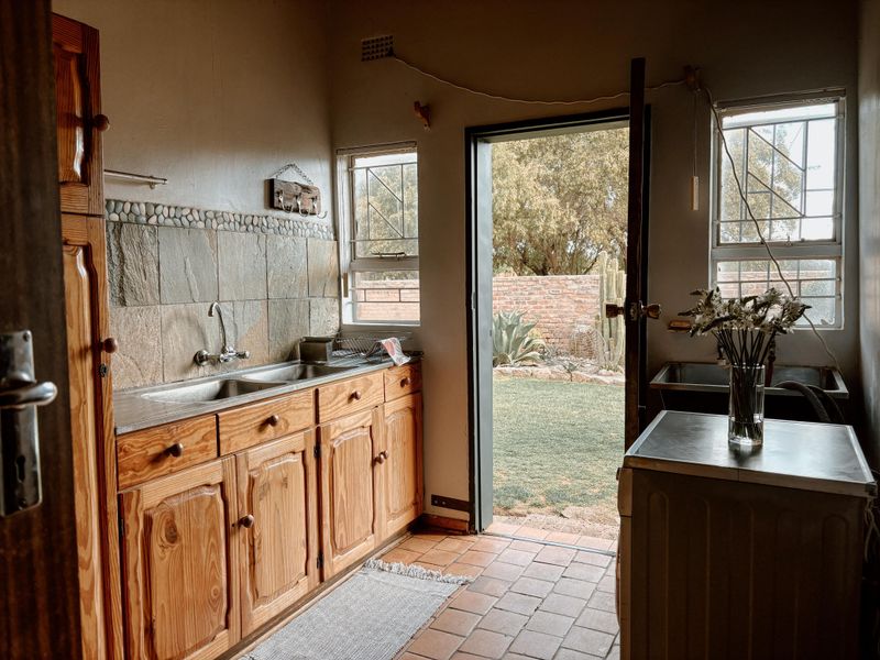 A functional laundry area featuring wooden cabinetry, a double stainless steel sink, tiled flooring, and direct access to the rear garden.