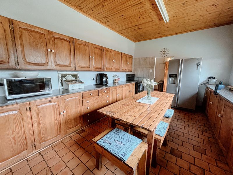 Spacious kitchen featuring extensive timber cabinetry, terracotta tiled flooring, and a natural wood ceiling, offering a rustic and functional cooking and dining space.