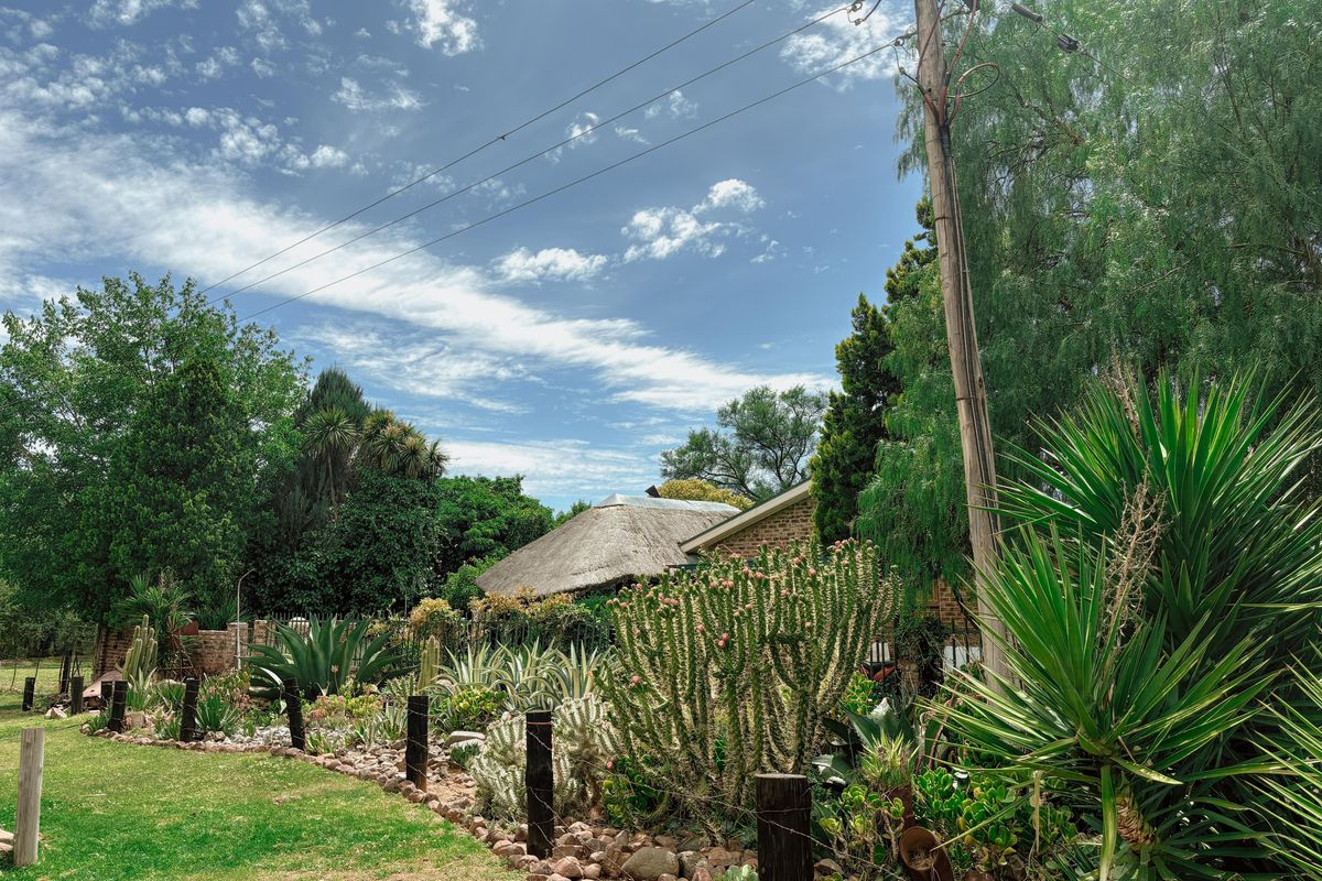A view of the property exterior featuring a landscaped garden with mature succulents and a traditional thatched roof structure in the background.