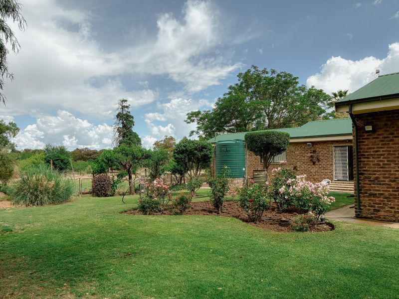 A well-maintained rear garden featuring a lush lawn, established rose beds, and a green water storage tank adjacent to the brick house exterior.