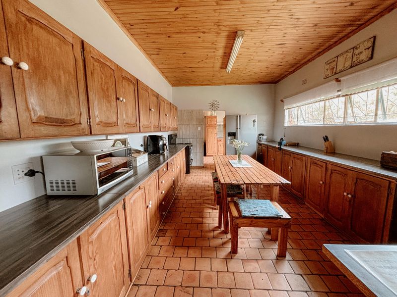 Spacious kitchen featuring extensive wooden cabinetry, terracotta tiled flooring, and a timber-clad ceiling, offering a traditional aesthetic with ample storage and workspace.