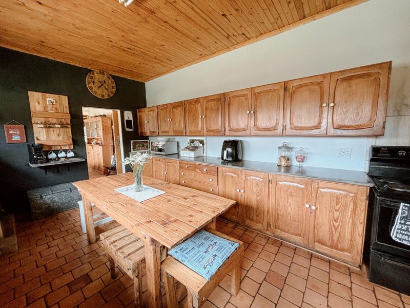 A rustic kitchen featuring wooden cabinetry, a timber-clad ceiling, and terracotta floor tiles, providing a warm and traditional cooking space.