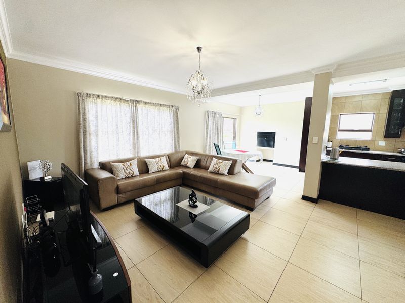 Spacious open-plan living area featuring tiled floors, a modern kitchen with granite countertops, and elegant chandelier lighting, creating a bright and functional home layout.