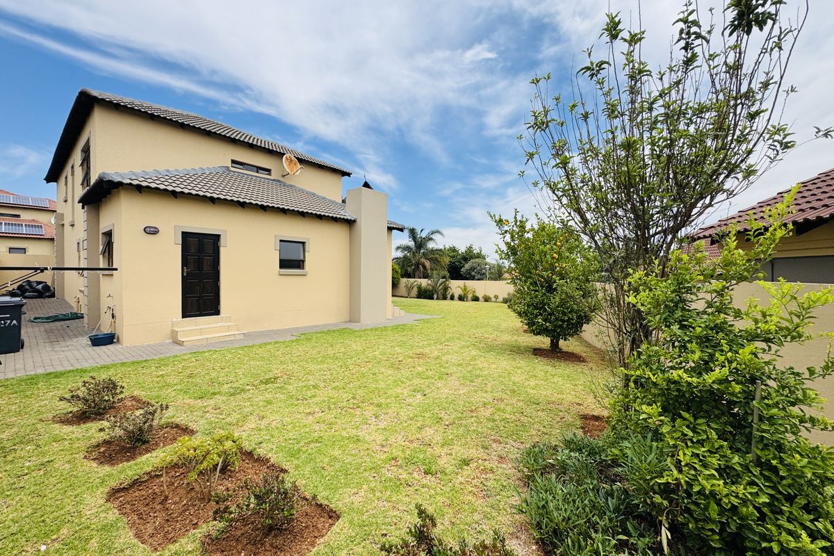 Rear view of the property featuring a well-maintained lawn, paved walkway, and perimeter boundary wall.