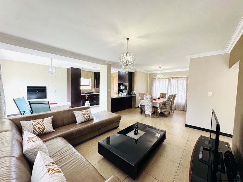 Spacious open-plan living and dining area featuring tiled floors, crown molding, and a modern kitchen with dark cabinetry and a central island.