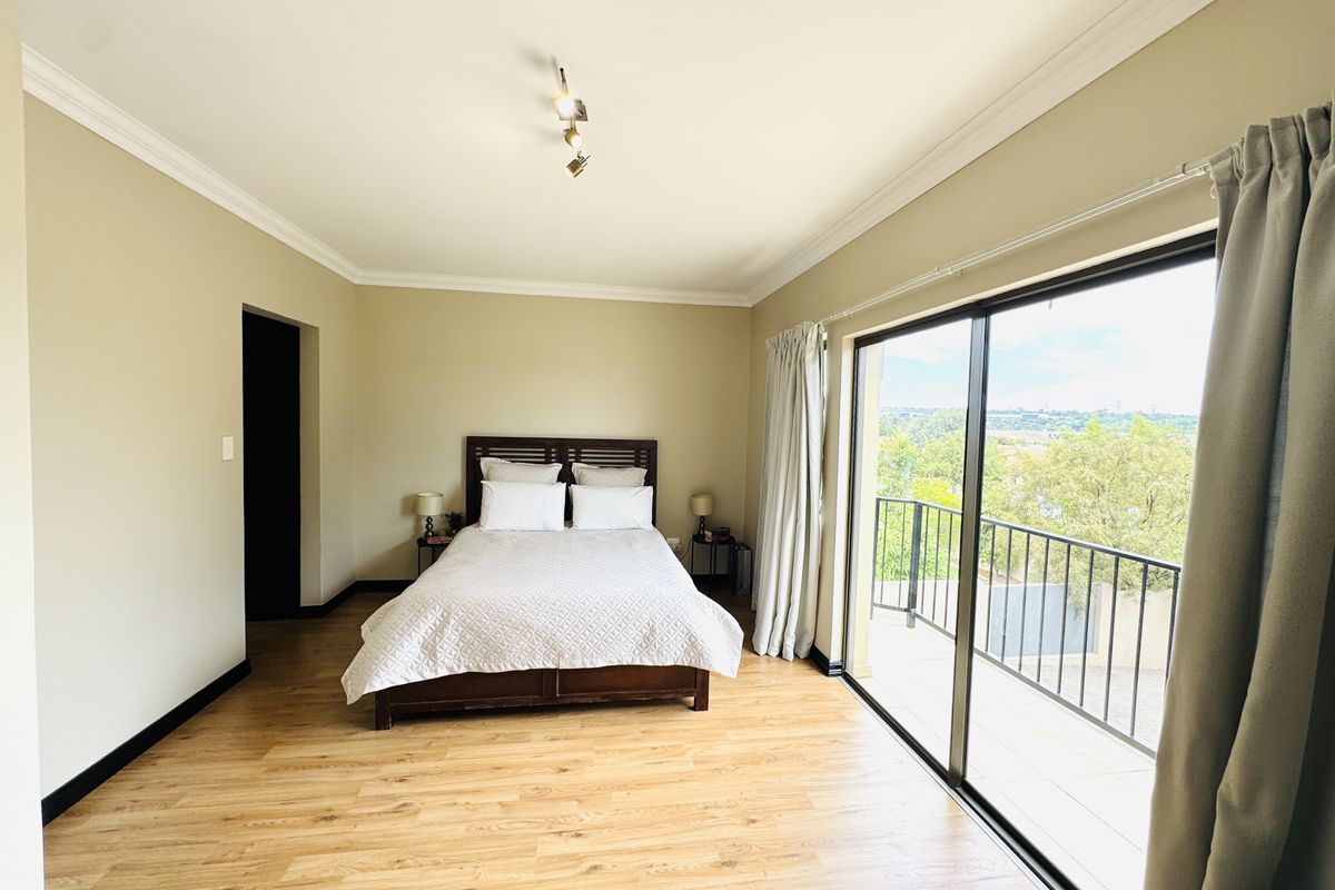 Spacious bedroom featuring light laminate flooring, crown molding, and a large sliding glass door opening onto a private balcony with scenic views.