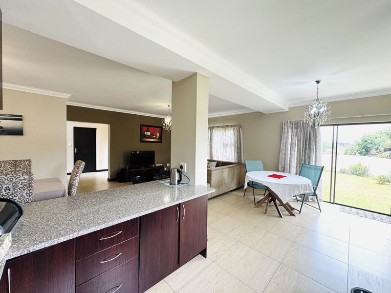 Spacious open-plan living and dining area featuring tiled floors, modern kitchen cabinetry with granite countertops, and sliding doors leading to the garden.