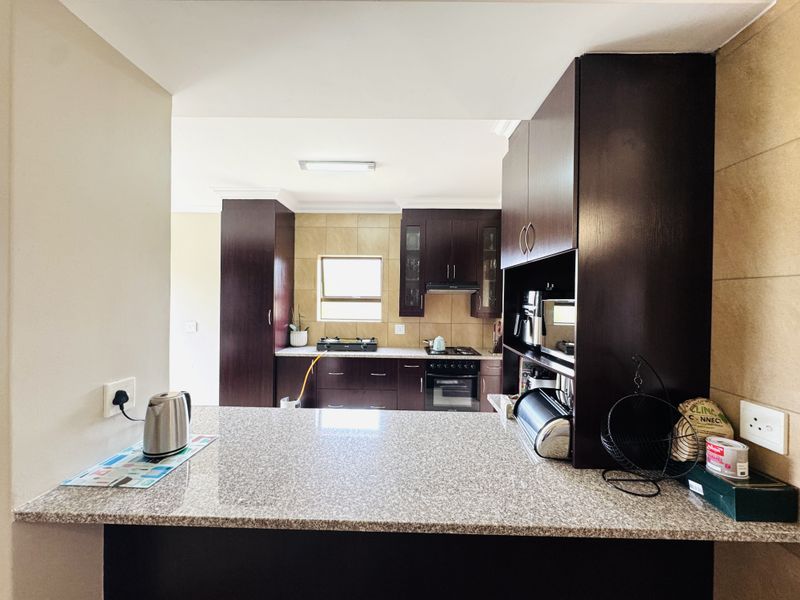 A functional kitchen featuring dark wood cabinetry, granite countertops, a breakfast bar, and built-in cooking appliances with a tiled backsplash.