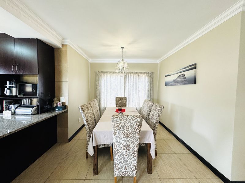 A well-maintained dining area featuring tiled flooring, crown molding, a decorative chandelier, and adjacent built-in cabinetry with granite countertops.